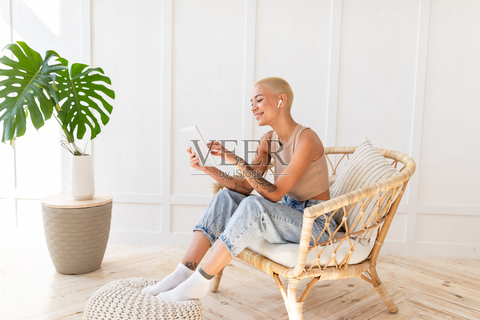 女士使用数码平板电脑和无线耳机，休息在白色墙壁的柳条椅，复制空间照片摄影图片