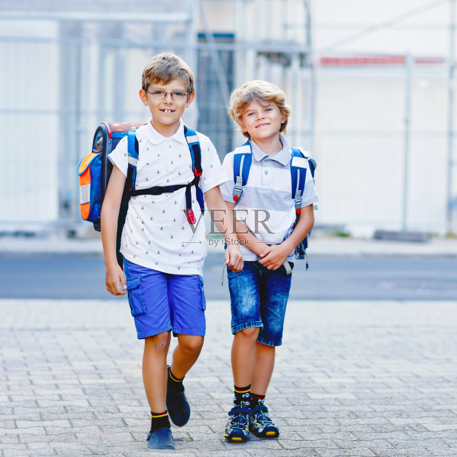两个小男孩背着背包或背包。孩子们在上学的路上。健康可爱的孩子，兄弟和最好的朋友在户外离开家。回到学校。快乐的兄弟姐妹。照片摄影图片
