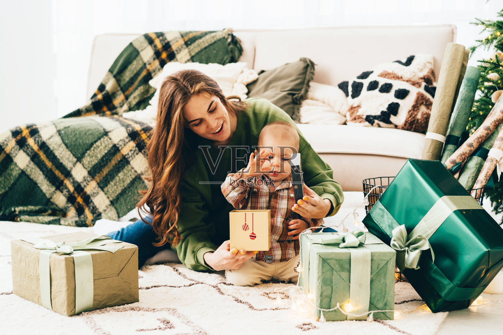 妈妈带着一个小孩子坐在客厅的地板上打开圣诞礼物盒。照片摄影图片