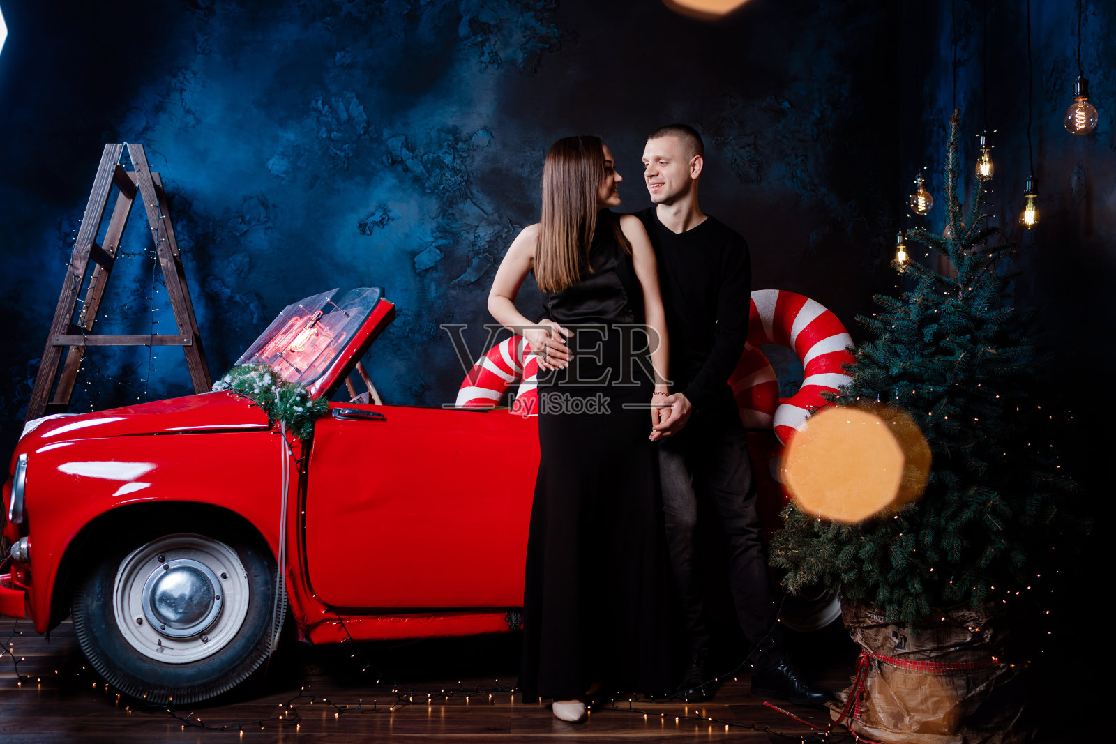 在圣诞节，一对幸福的年轻男女在一辆红色复古汽车旁抱着新年礼物。亲吻，女孩，幸福，检疫，圣诞节庆祝，节日。照片摄影图片