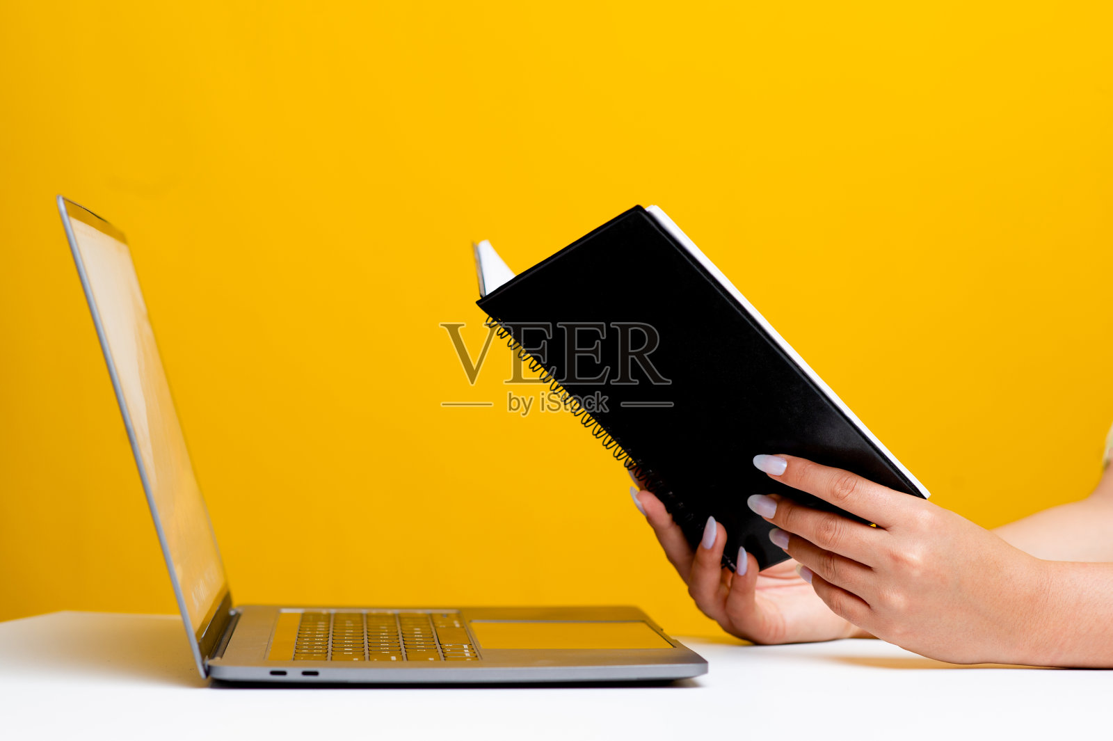 手和书侧视图阅读在一个白色的桌子在前面有一个笔记本电脑。书籍阅读概念放松阅读黄色背景照片摄影图片