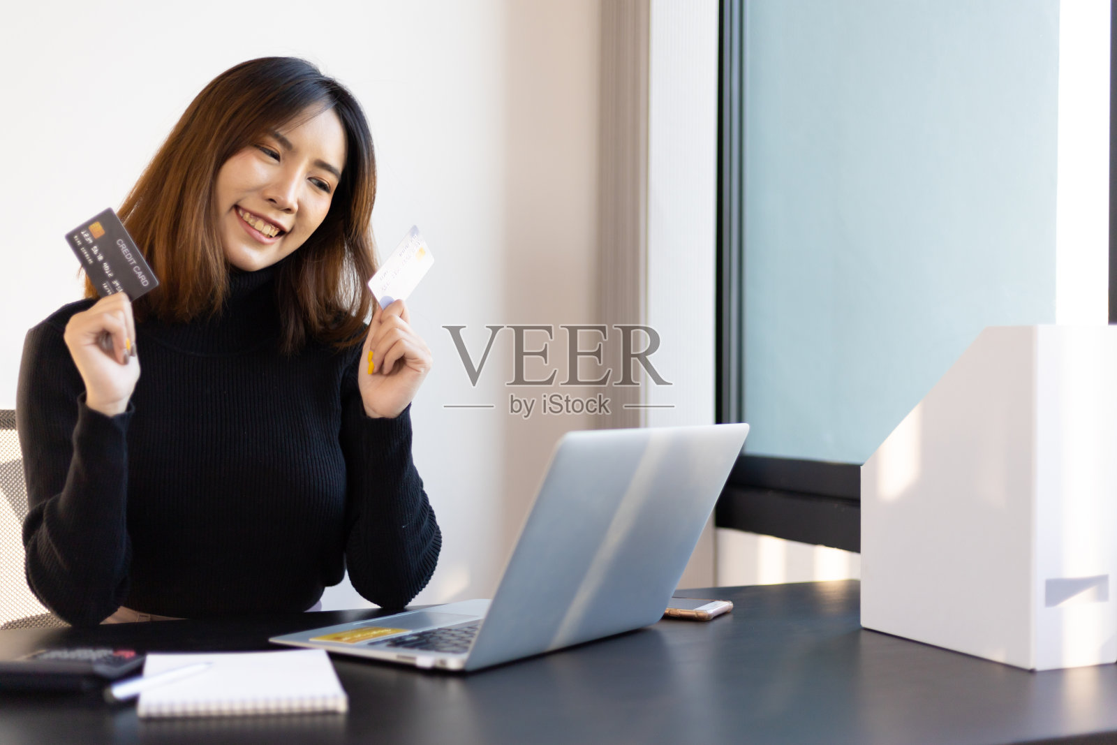 快乐微笑的亚洲妇女在办公室拿着信用卡。金融和网上购物概念。照片摄影图片