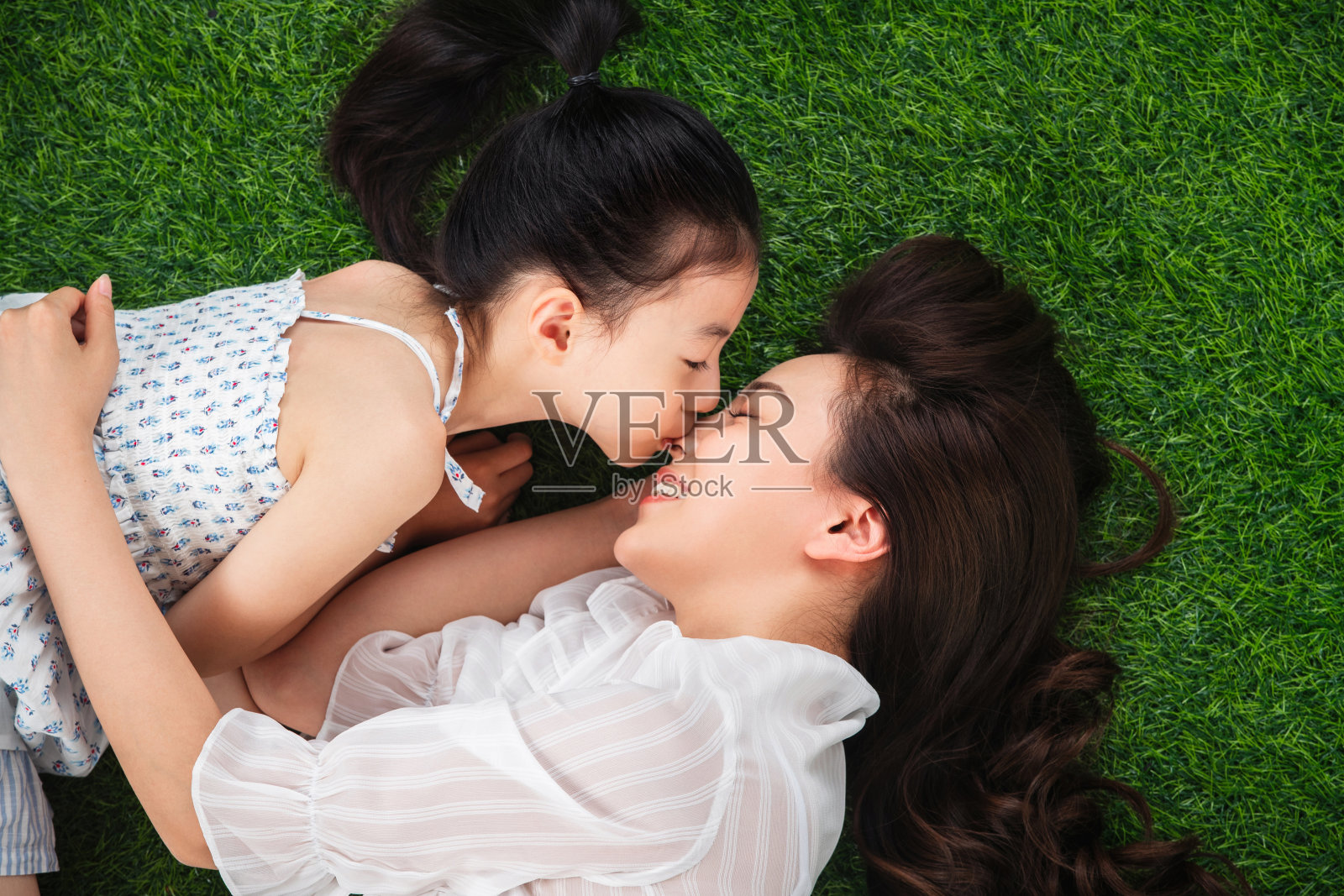 草地上小女孩亲吻母亲照片摄影图片
