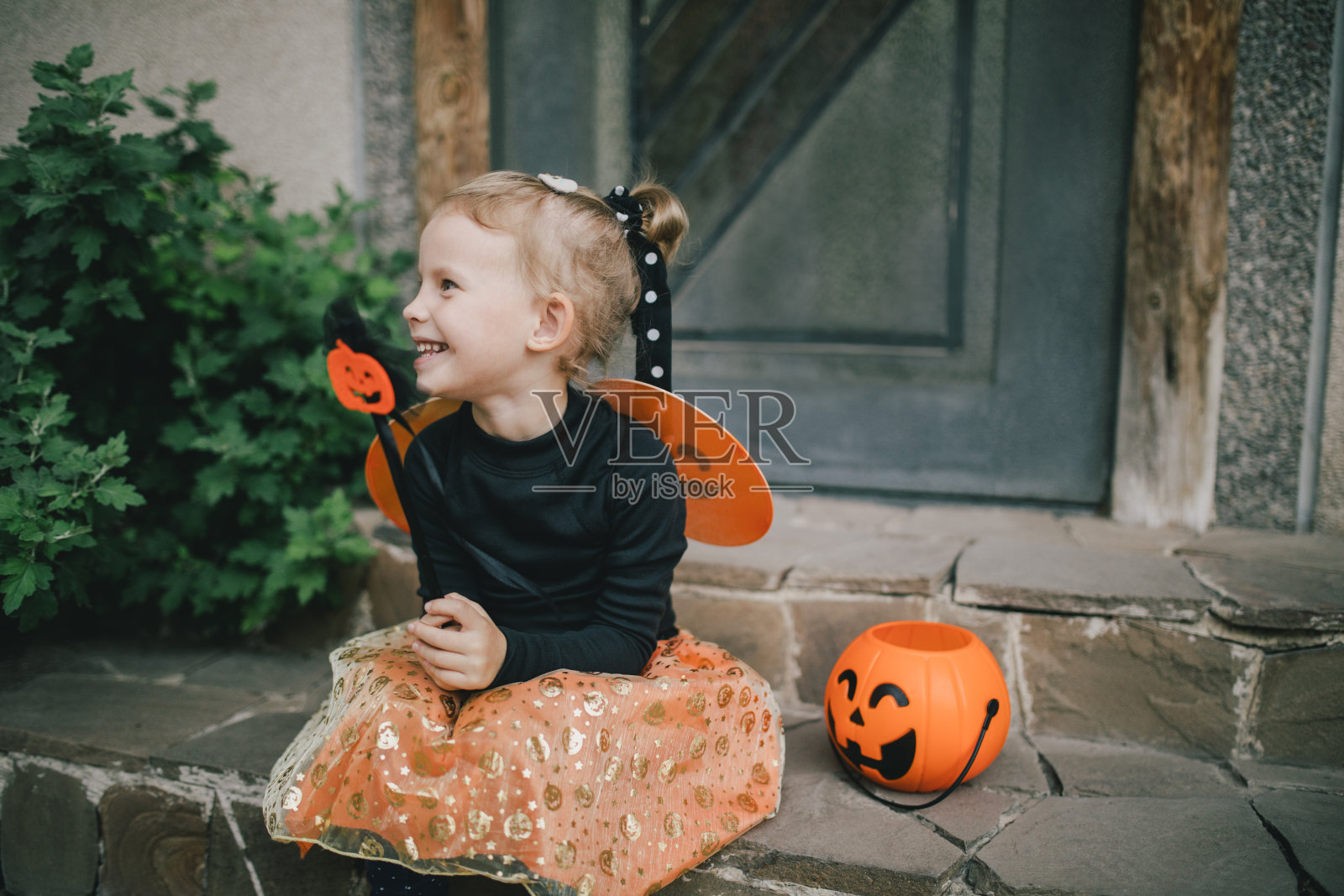 万圣节那天，可爱的小女孩穿着女巫服装，拿着南瓜桶和糖果。不给糖就捣蛋。照片摄影图片