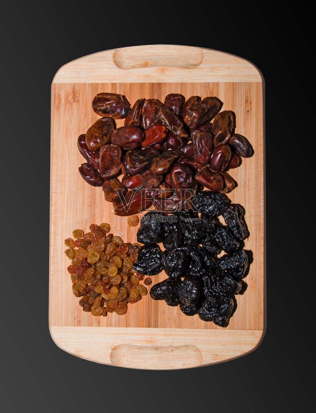 一把干枣、葡萄干和梅干放在厨房的木板上。干果的背景。健康食品的概念。在黑色背景上隔离。照片摄影图片