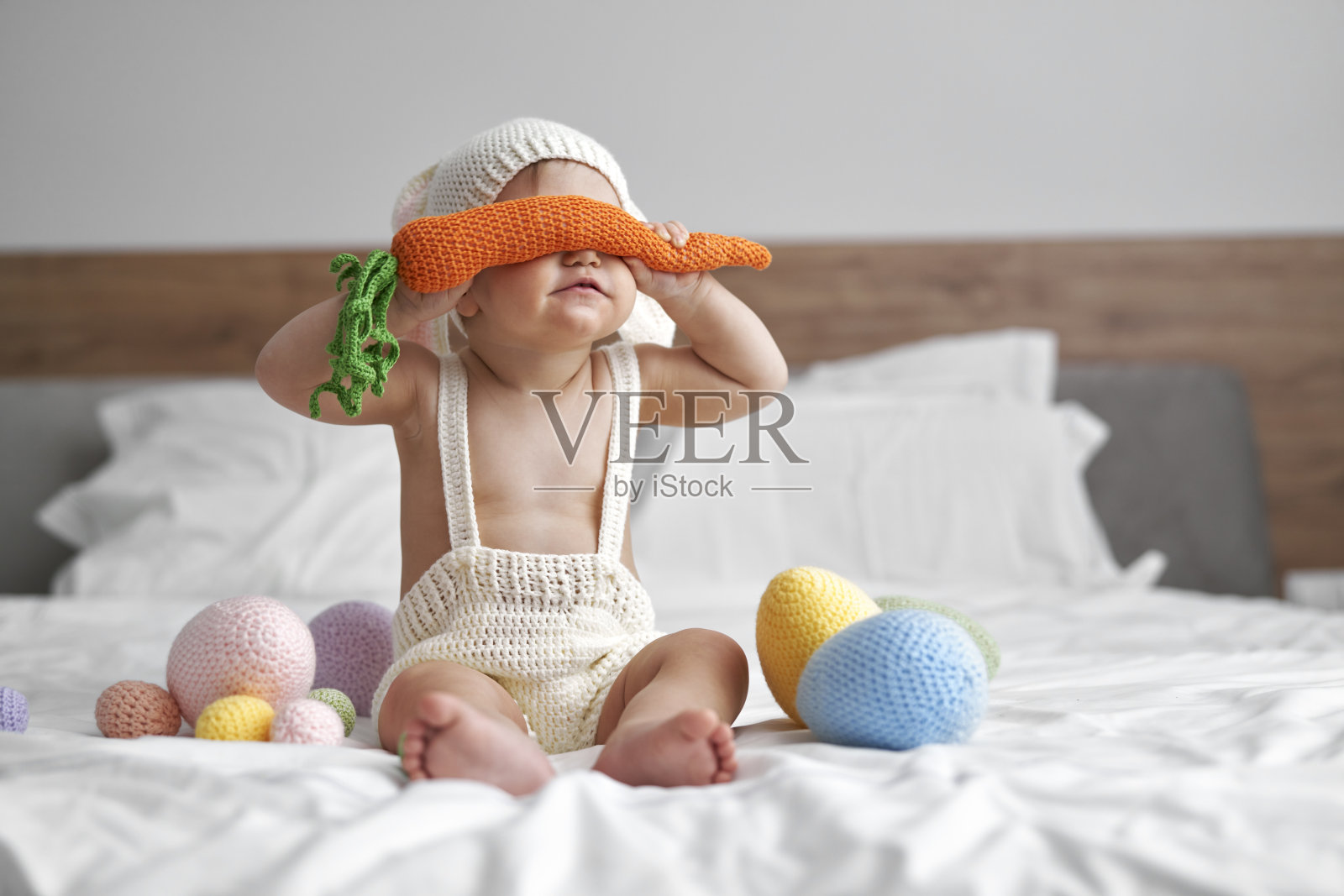 穿着兔子服装的小婴儿用大胡萝卜遮住眼睛照片摄影图片