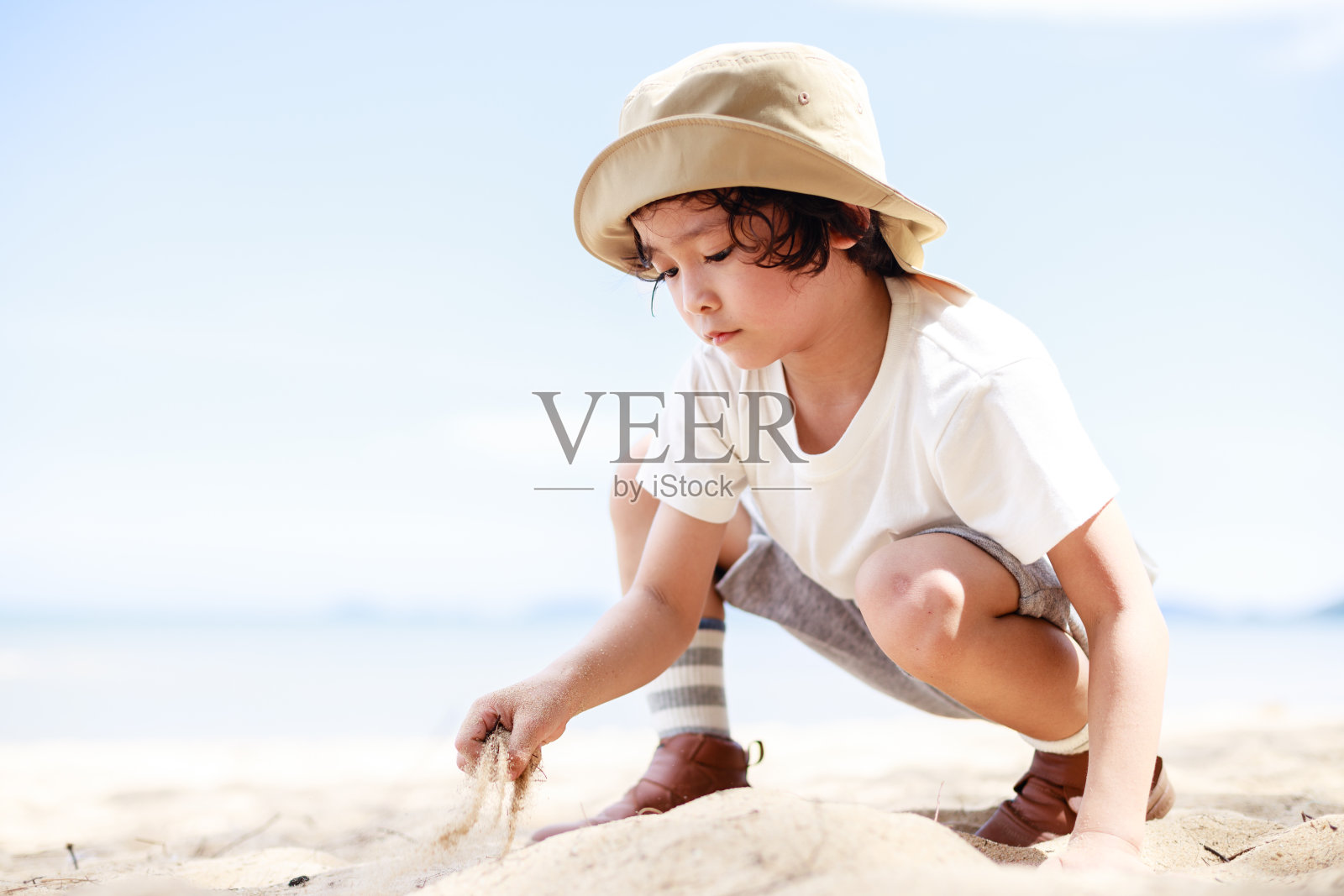 戴着帽子的孩子在海边的沙滩上玩沙子。和孩子们在海边度假照片摄影图片