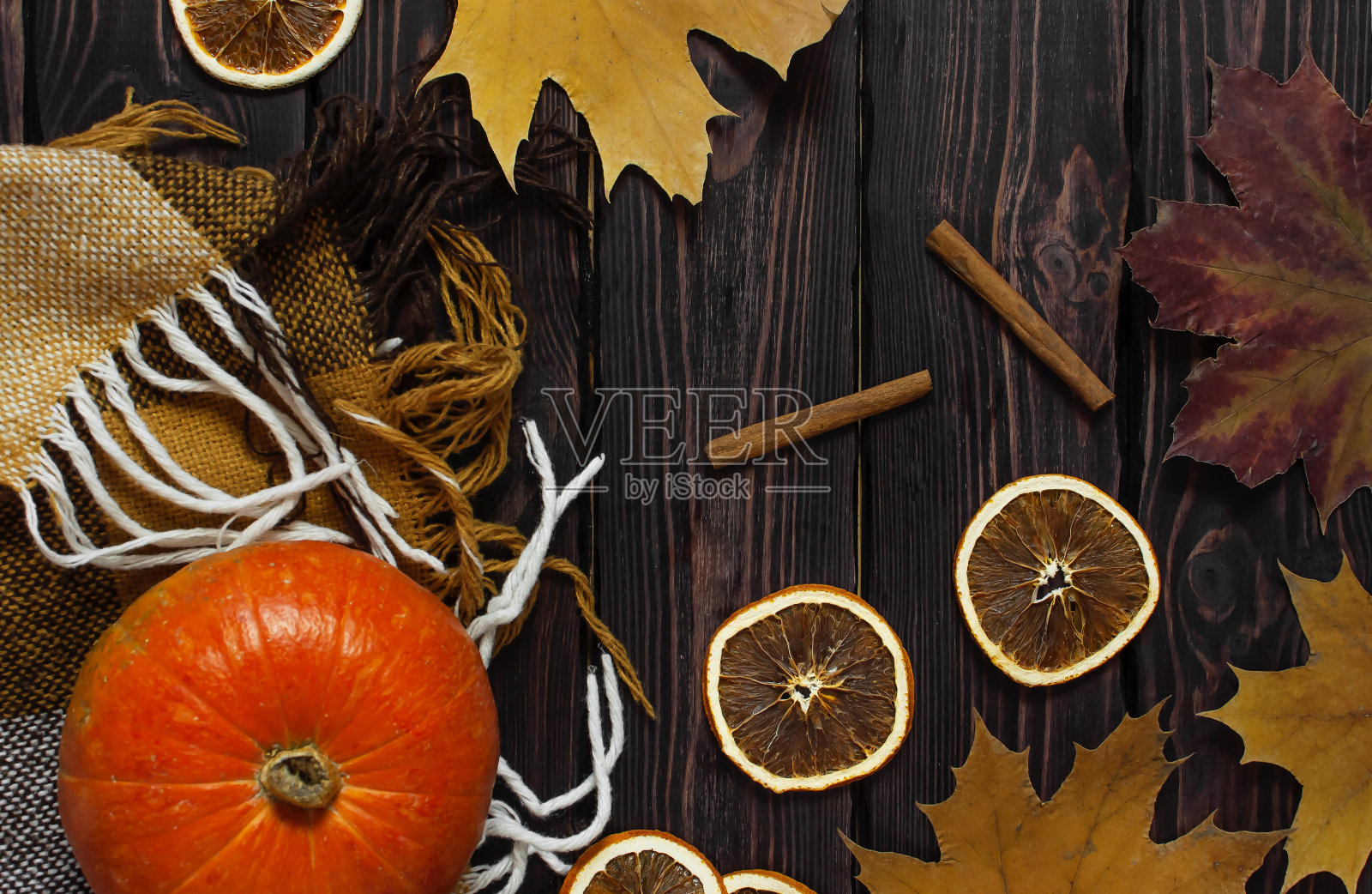 橙色南瓜，肉桂，干橙片，秋天的彩色树叶和格子格在一个深色的木制背景顶部视图与文字的空间。秋季南瓜感恩节背景。照片摄影图片