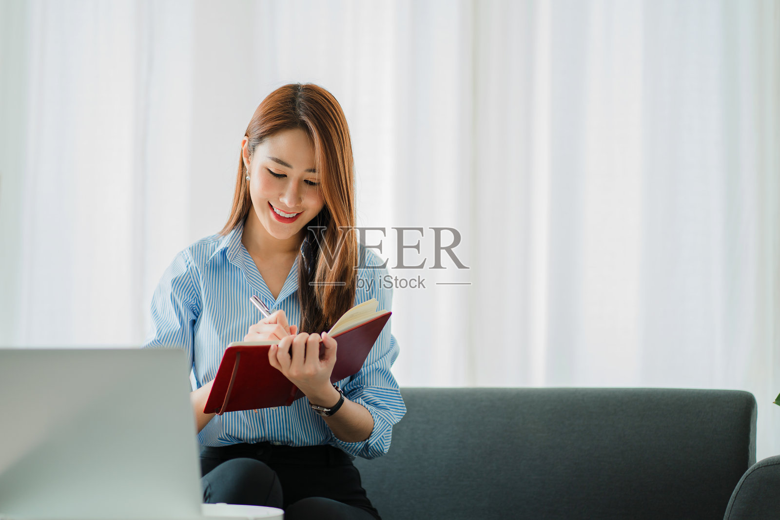 亚洲女性在家里用笔记本电脑坐在沙发上在线工作的概念照片摄影图片